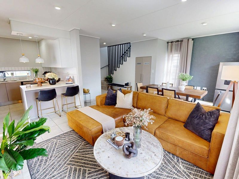Modern open-plan living area featuring a sleek kitchen with island, dining space, and staircase, finished with contemporary neutral tones and recessed lighting.