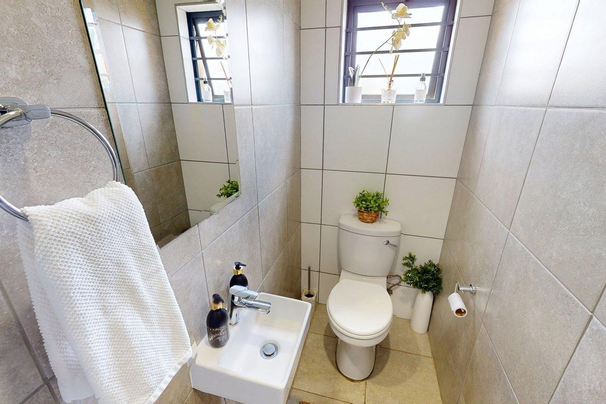 A compact, modern guest bathroom featuring neutral wall and floor tiles, a wall-mounted basin, and a standard toilet.