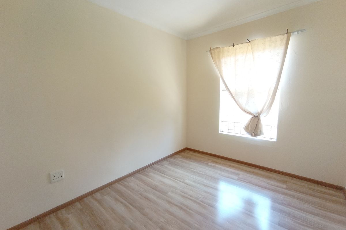 A bright, empty bedroom featuring light-toned laminate flooring, neutral walls, and a window with security bars.