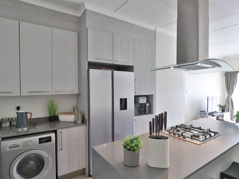 Modern kitchen featuring light wood-grain cabinetry, stone countertops, a central island with a gas hob, and an integrated washing machine.