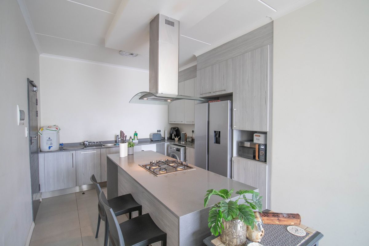 Modern kitchen featuring a central island with a gas hob, stainless steel extractor fan, ample built-in cabinetry, and stone countertops.