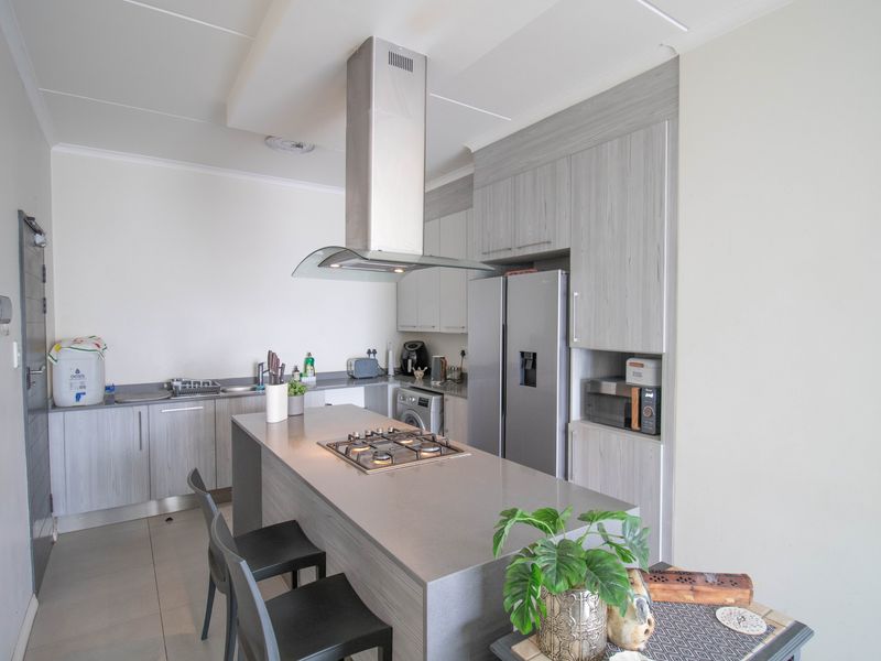 Modern kitchen featuring a central island with a gas hob, stainless steel extractor fan, ample built-in cabinetry, and stone countertops.
