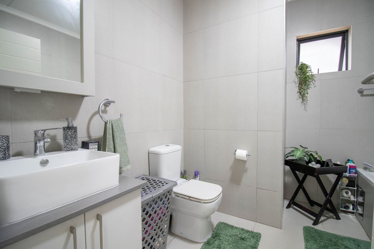 A modern, well-maintained bathroom featuring neutral wall tiles, a contemporary vanity with a countertop basin, and a functional toilet.