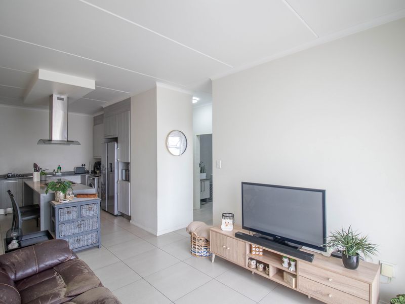 An open-plan living and kitchen area featuring modern tiled flooring, a central kitchen island, and a sleek stainless steel extractor fan.