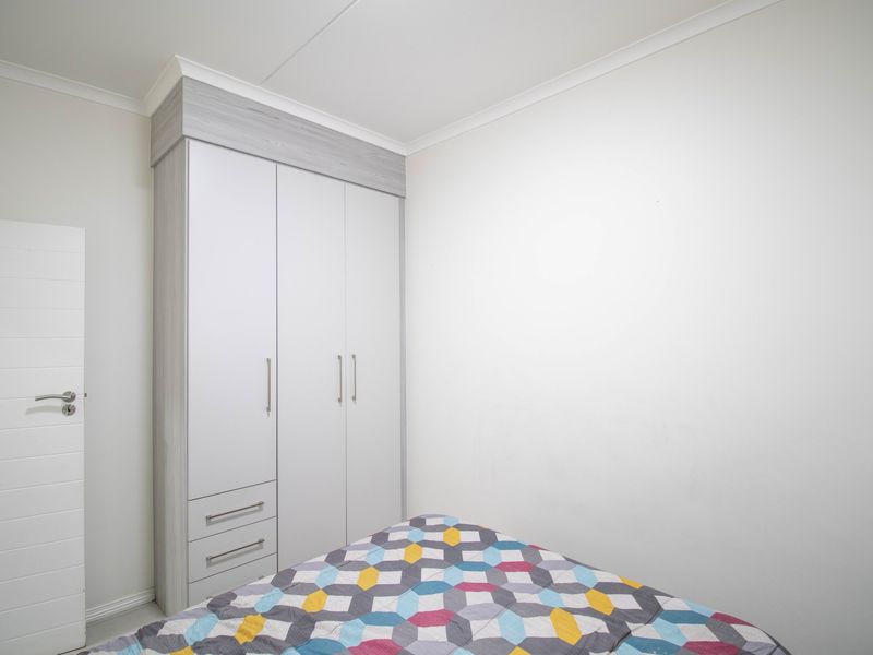 A clean, well-maintained bedroom featuring a modern built-in wardrobe with integrated drawers and neutral wall finishes.