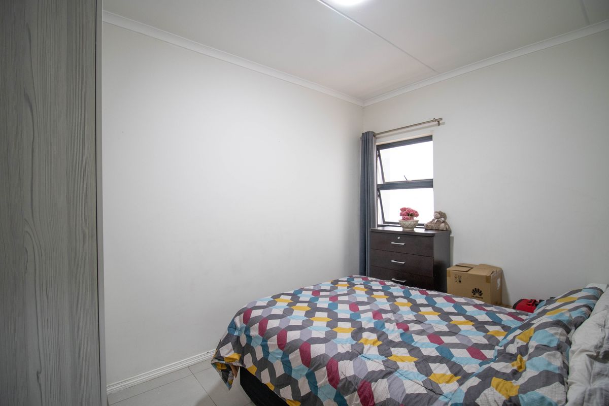 A functional bedroom featuring tiled flooring, a built-in wardrobe, and a top-hung window providing natural light.