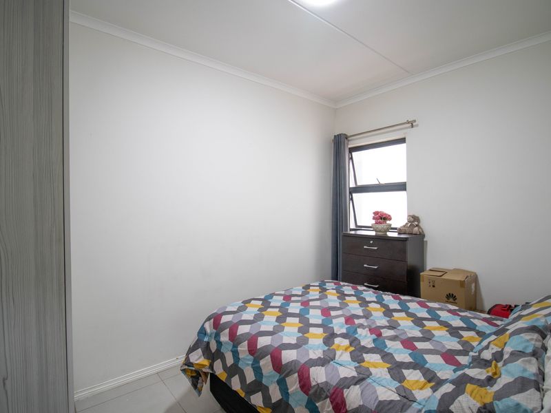 A functional bedroom featuring tiled flooring, a built-in wardrobe, and a top-hung window providing natural light.