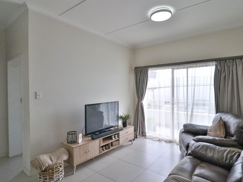 A bright living room featuring neutral tiled flooring and a large sliding glass door that provides access to the balcony.