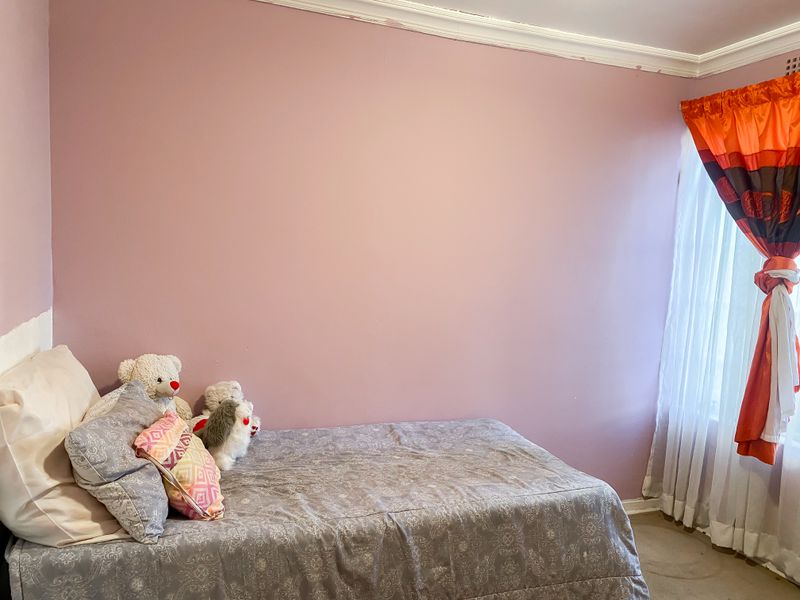 A bedroom featuring pink painted walls with visible paint application issues along the ceiling cornice and skirting boards.