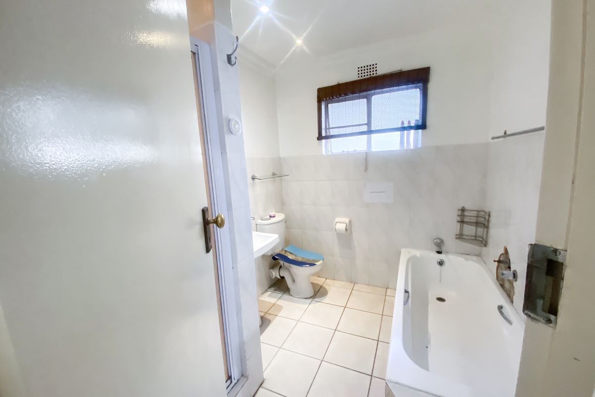 A functional bathroom featuring a bathtub, pedestal sink, and toilet, with tiled walls and flooring. The space requires minor repairs to wall finishes.