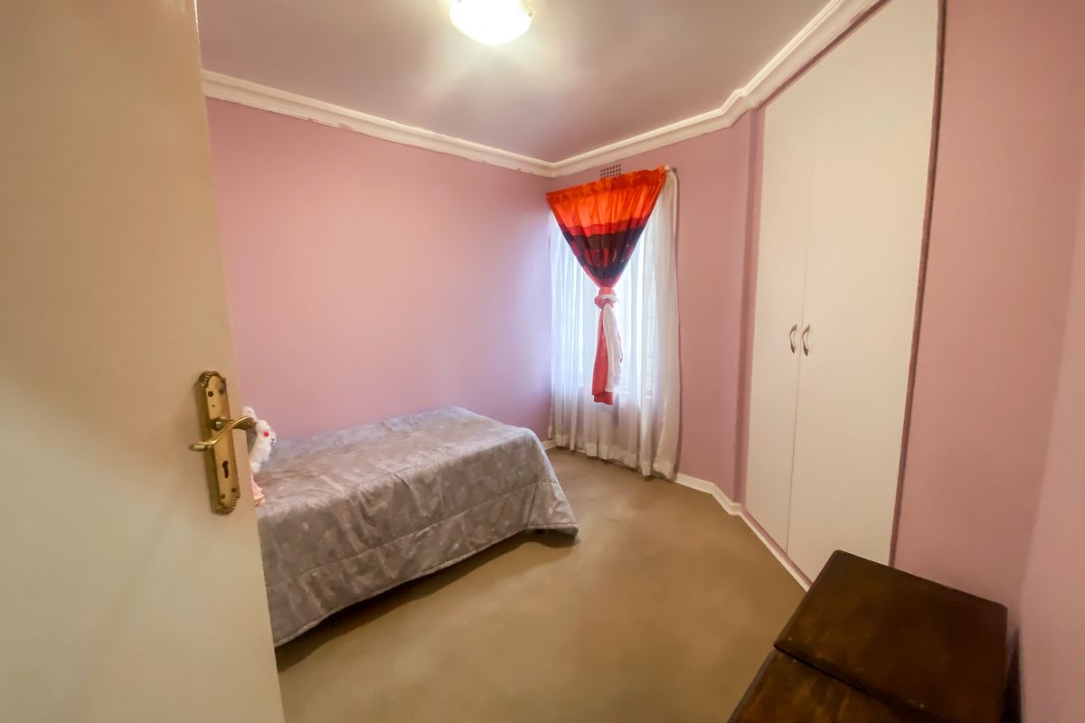A bedroom featuring pink walls, a built-in wardrobe, and a window with natural light.