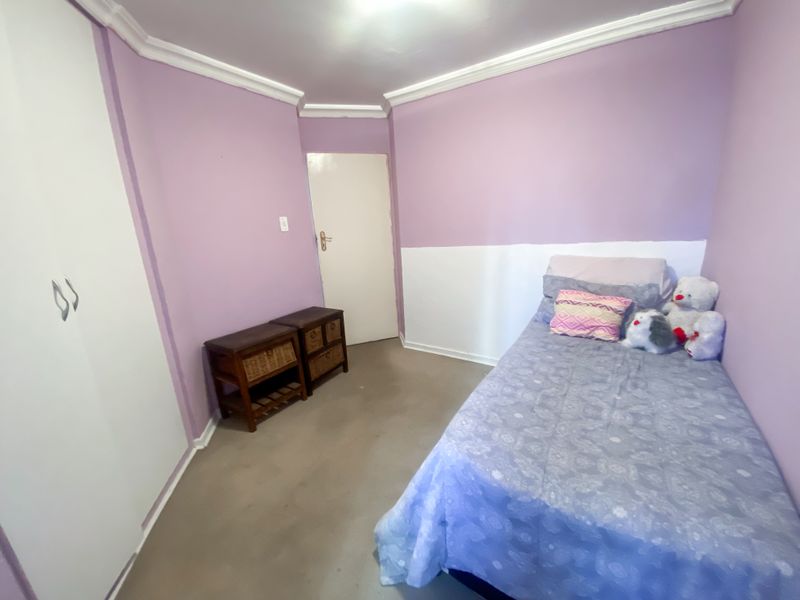 A bedroom featuring built-in wardrobes, decorative cornice detailing, and neutral flooring, offering a functional space with potential for modern updates.