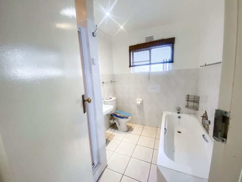 A functional bathroom featuring a bathtub, pedestal sink, and toilet, with tiled walls and flooring. The space requires minor repairs to wall finishes.
