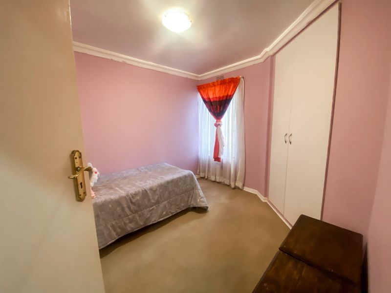 A bedroom featuring pink walls, a built-in wardrobe, and a window with natural light.