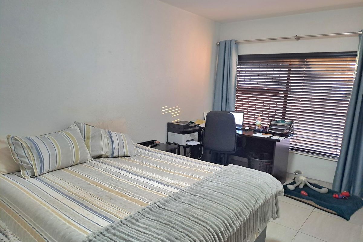 A bedroom featuring tiled flooring and a window fitted with horizontal blinds and curtain rods.
