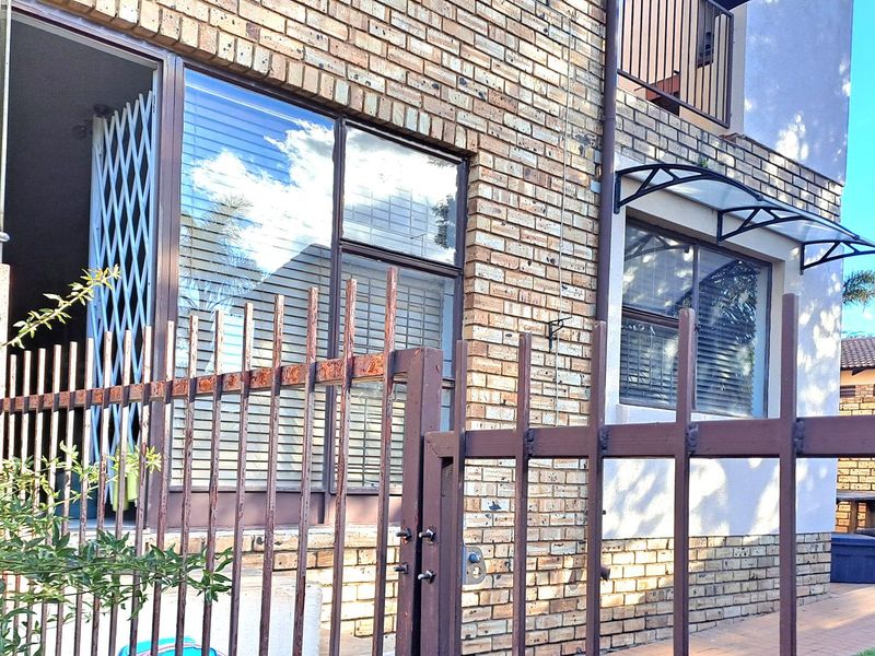 Exterior view of an apartment building featuring face-brick facade, metal security gates, and window awnings.
