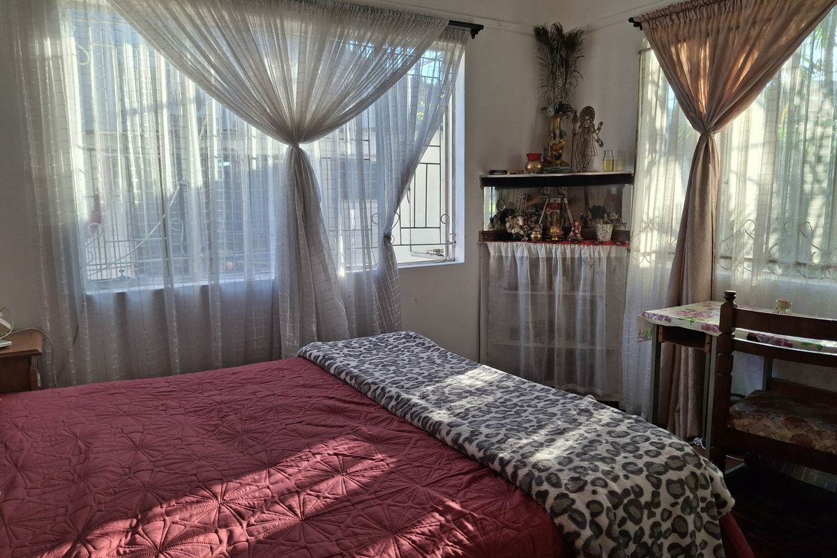 A sunlit bedroom featuring large windows with security bars and neutral wall finishes, offering a comfortable and functional living space.
