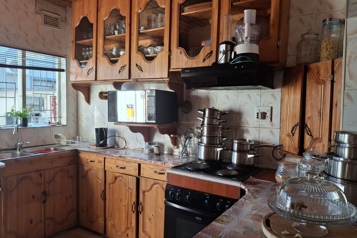 A functional kitchen featuring traditional wooden cabinetry, an electric stove with extractor fan, and a double sink with tiled backsplash.