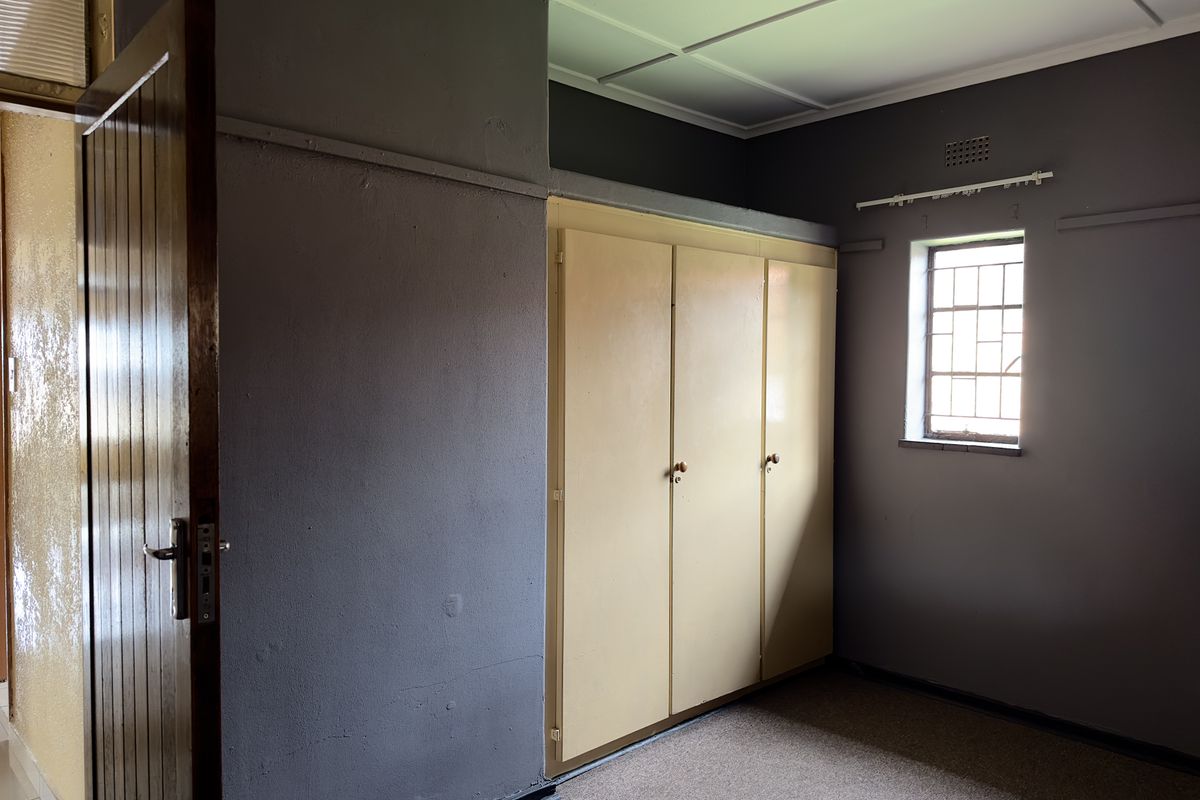 A bedroom featuring built-in storage cabinetry, a window with security bars, and carpeted flooring.