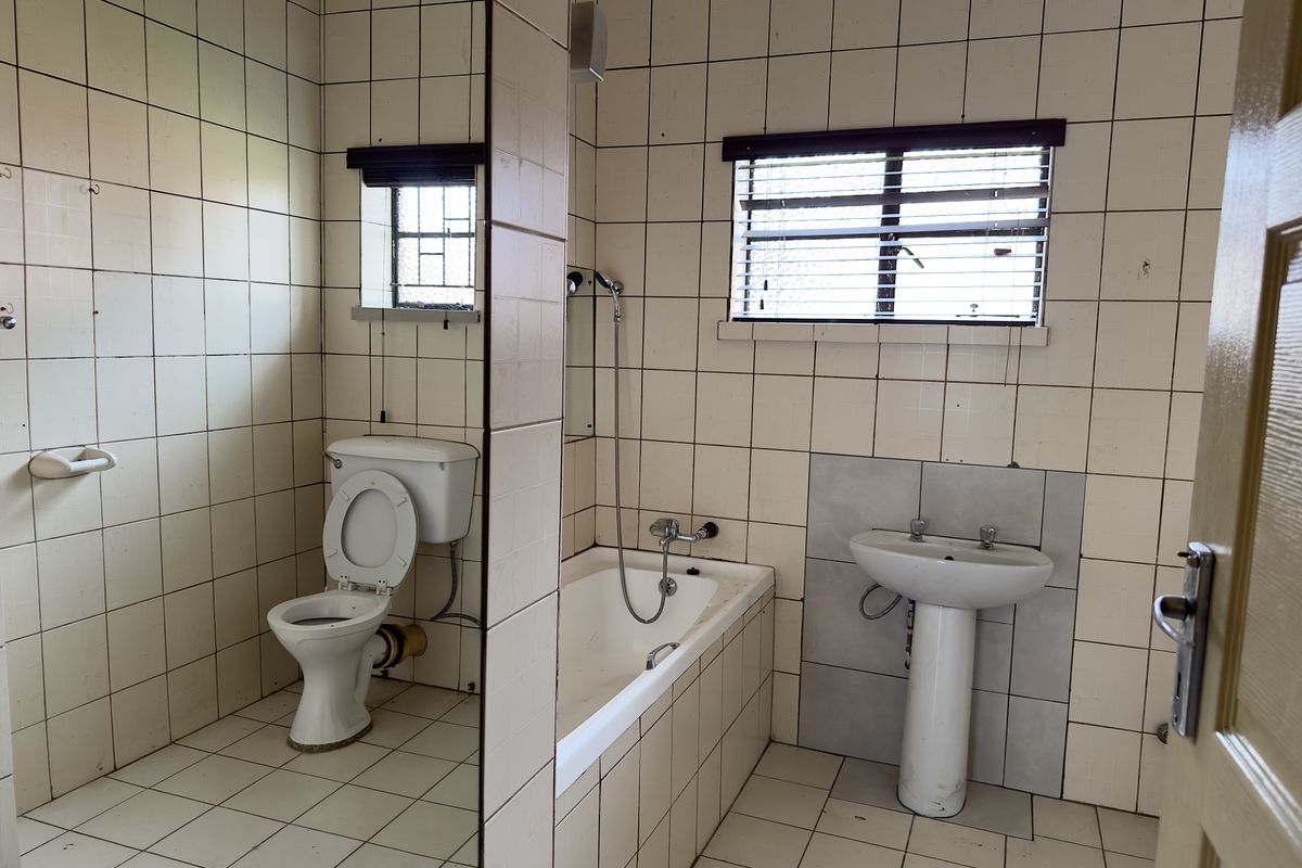 A dated bathroom featuring a pedestal basin, bathtub with shower mixer, and toilet, finished with full-height wall and floor tiling.
