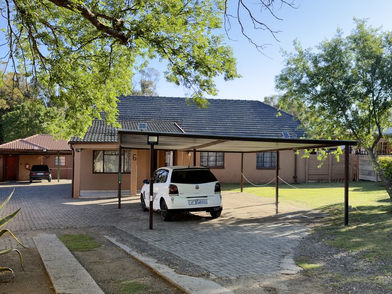 Front exterior view of the house featuring a paved driveway, a covered carport, and a tiled roof structure.