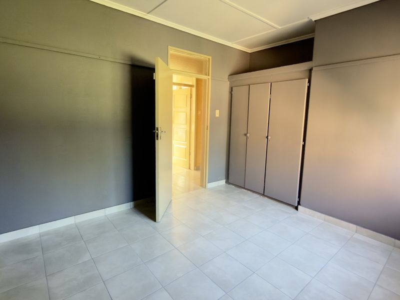 A clean, empty bedroom featuring neutral grey walls, tiled flooring, and built-in cupboards, offering a versatile space ready for personalization.