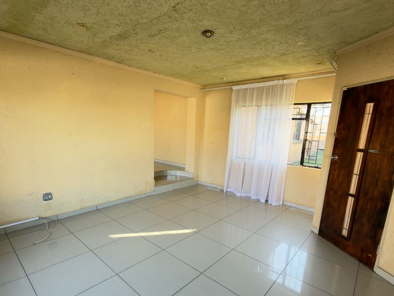 An empty living room featuring tiled flooring, recessed lighting, and a wooden entrance door, requiring cosmetic updates to the walls and ceiling.