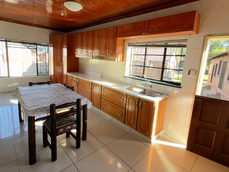 A functional kitchen featuring wooden cabinetry, tiled flooring, and a timber ceiling, with direct access to the exterior.