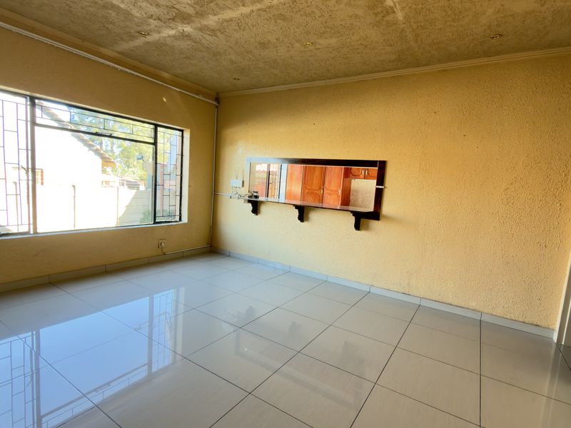 An empty living room featuring polished tiled flooring, large windows with security bars, and a built-in wall mirror.