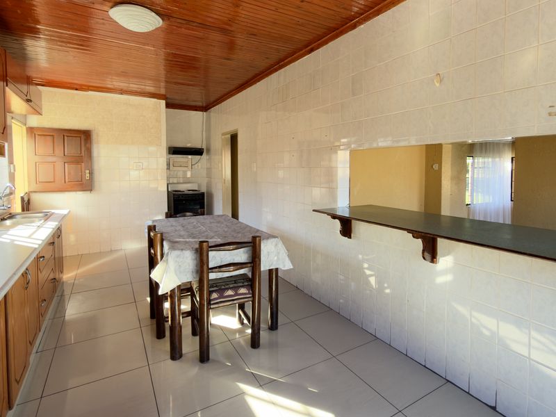 A functional kitchen featuring wooden cabinetry, tiled walls, and a breakfast bar, with a traditional wooden ceiling and tiled flooring throughout.