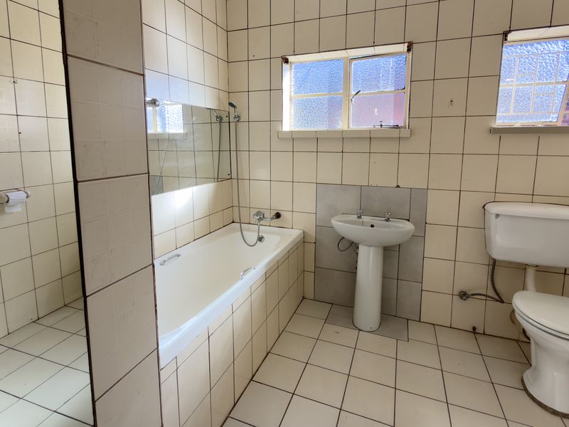 A dated bathroom featuring a bathtub, pedestal basin, and toilet with original tiled finishes, offering significant potential for a modern renovation.
