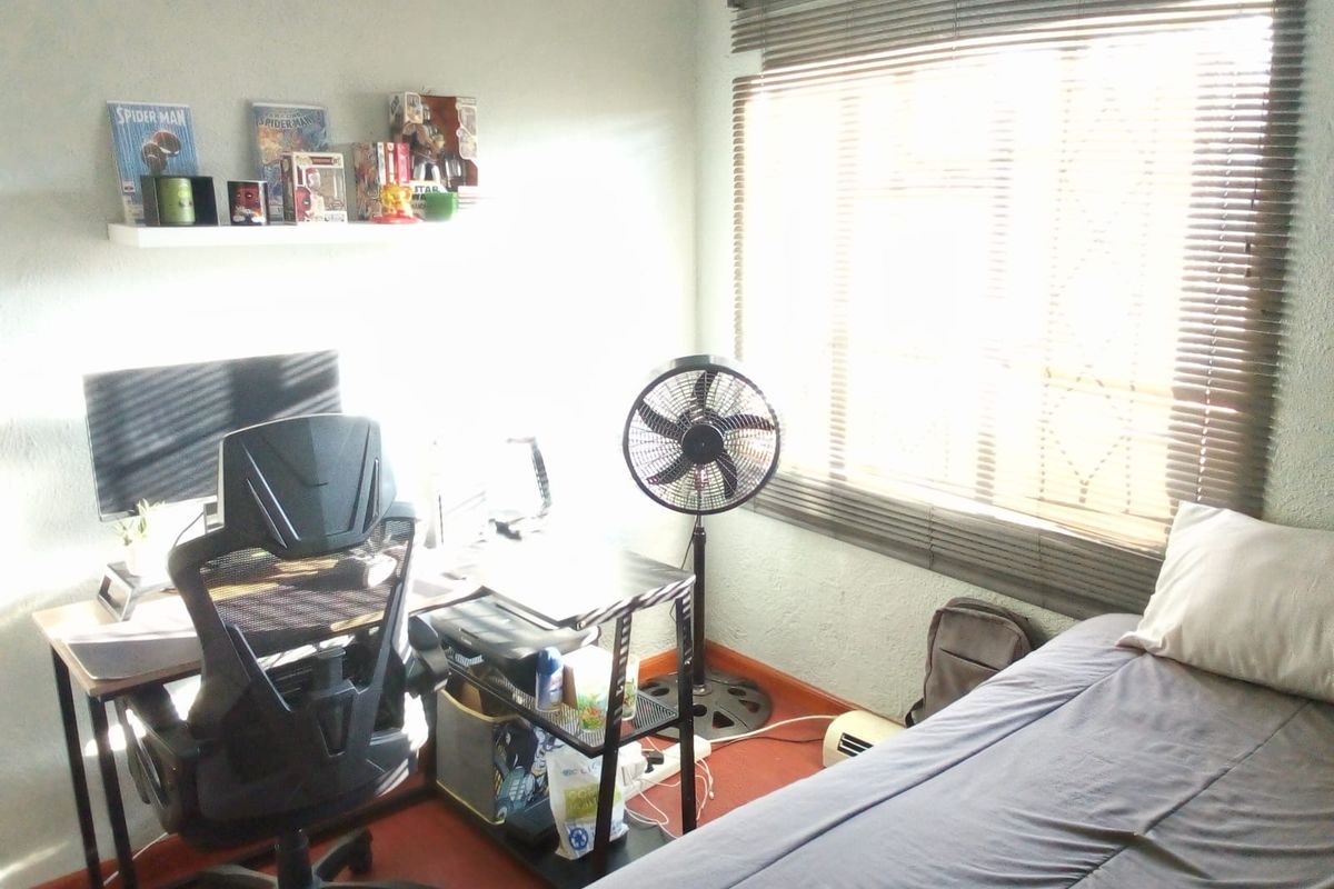 A bedroom featuring a window with venetian blinds and standard skirting boards, currently utilized as a home office and sleeping space.