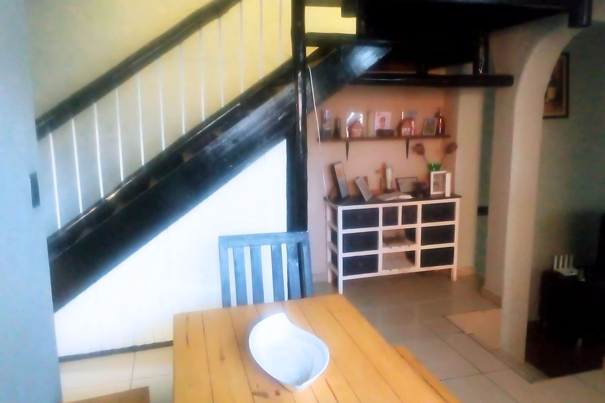 A living area featuring a staircase and tiled flooring, with an open-plan layout leading to an adjacent space through an archway.