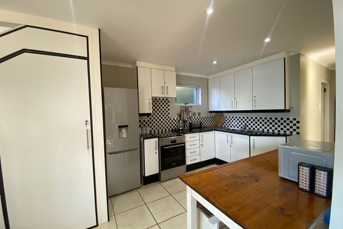 A functional kitchen featuring white cabinetry, a distinctive checkerboard tile backsplash, ceramic floor tiles, and integrated cooking appliances.