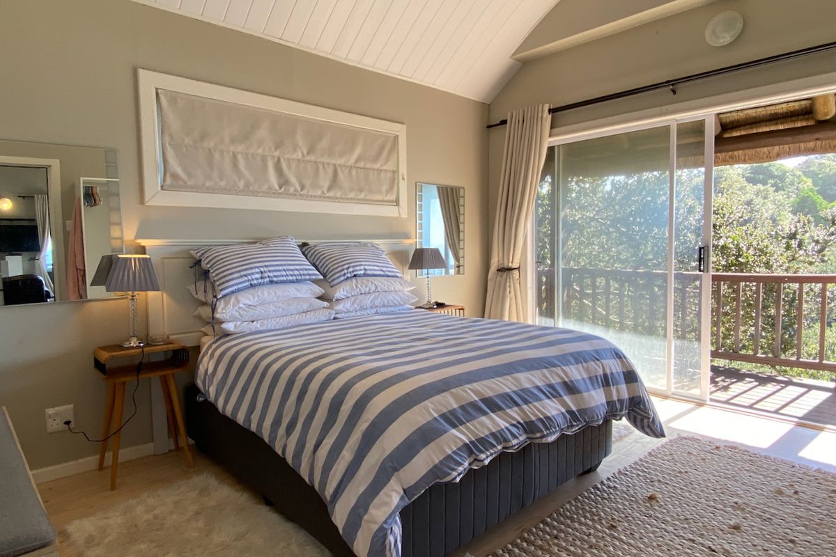 A bright bedroom featuring a vaulted timber ceiling, built-in headboard, and large sliding glass doors opening onto a private balcony with lush views.