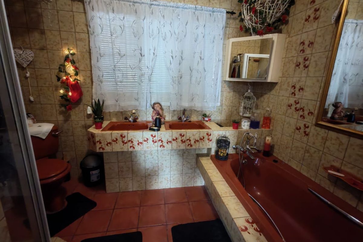 A dated bathroom featuring a double vanity, built-in bathtub, and shower enclosure with patterned wall tiles and terracotta-colored sanitaryware.