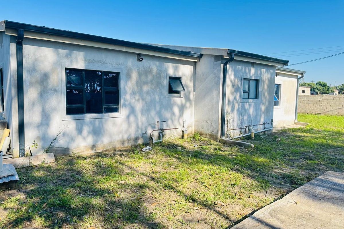 Rear view of the property showing unfinished exterior wall render, aluminium window frames, and exposed plumbing infrastructure set against a grassed yard.