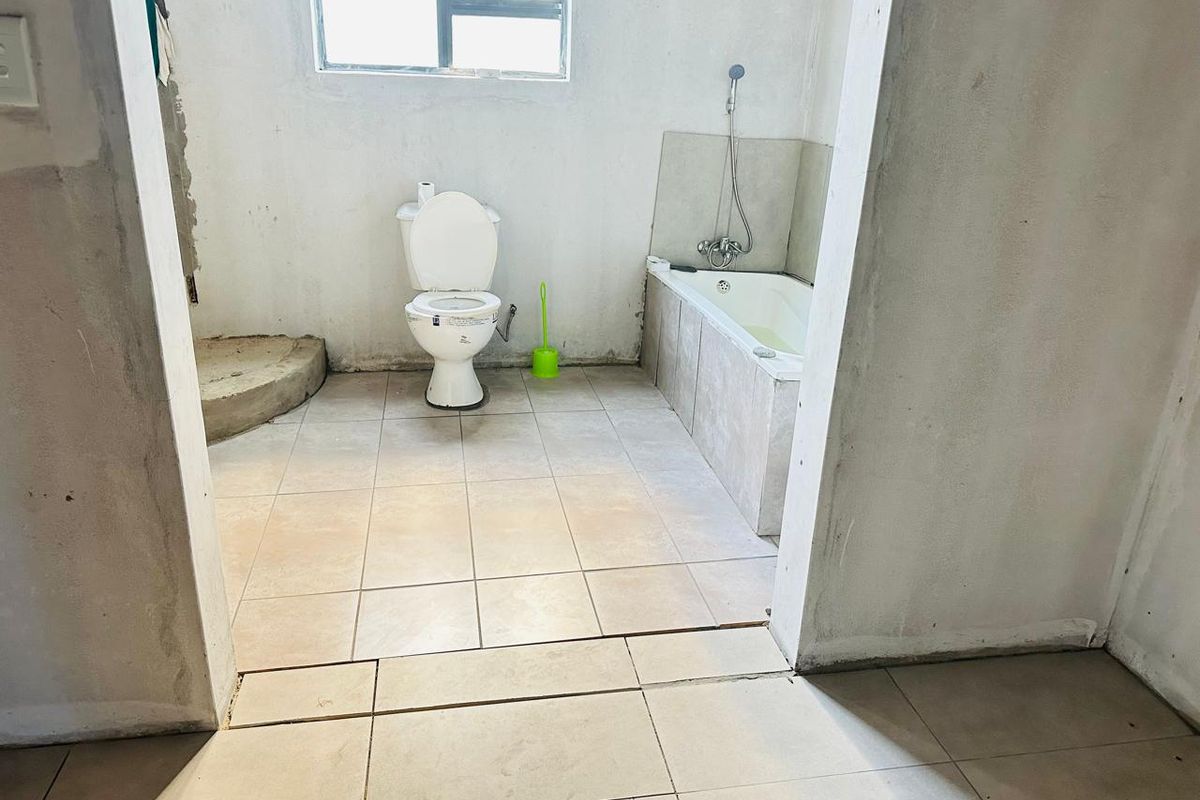 An unfinished bathroom featuring a toilet, bathtub with handheld shower mixer, and tiled flooring, currently requiring final plastering and finishing touches.