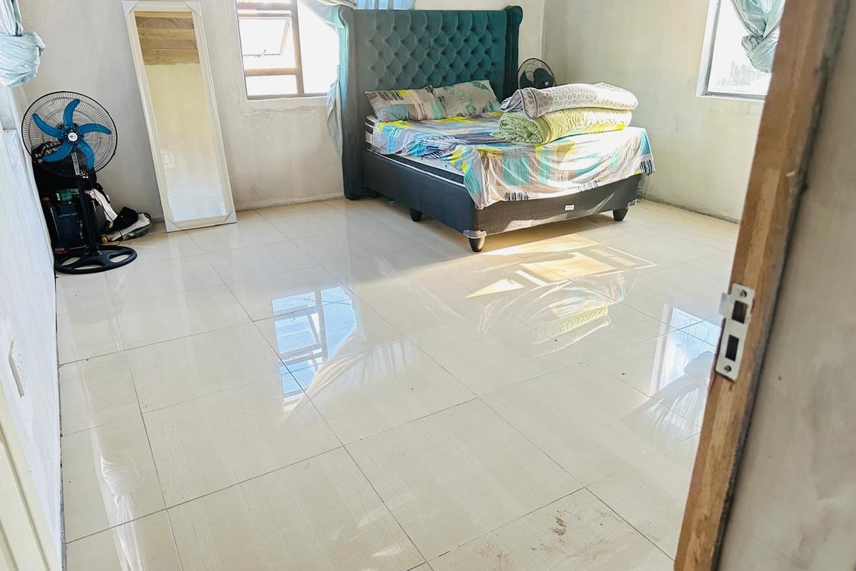 A bedroom featuring large format light-colored floor tiles and aluminium window frames, providing a blank canvas for interior design updates.