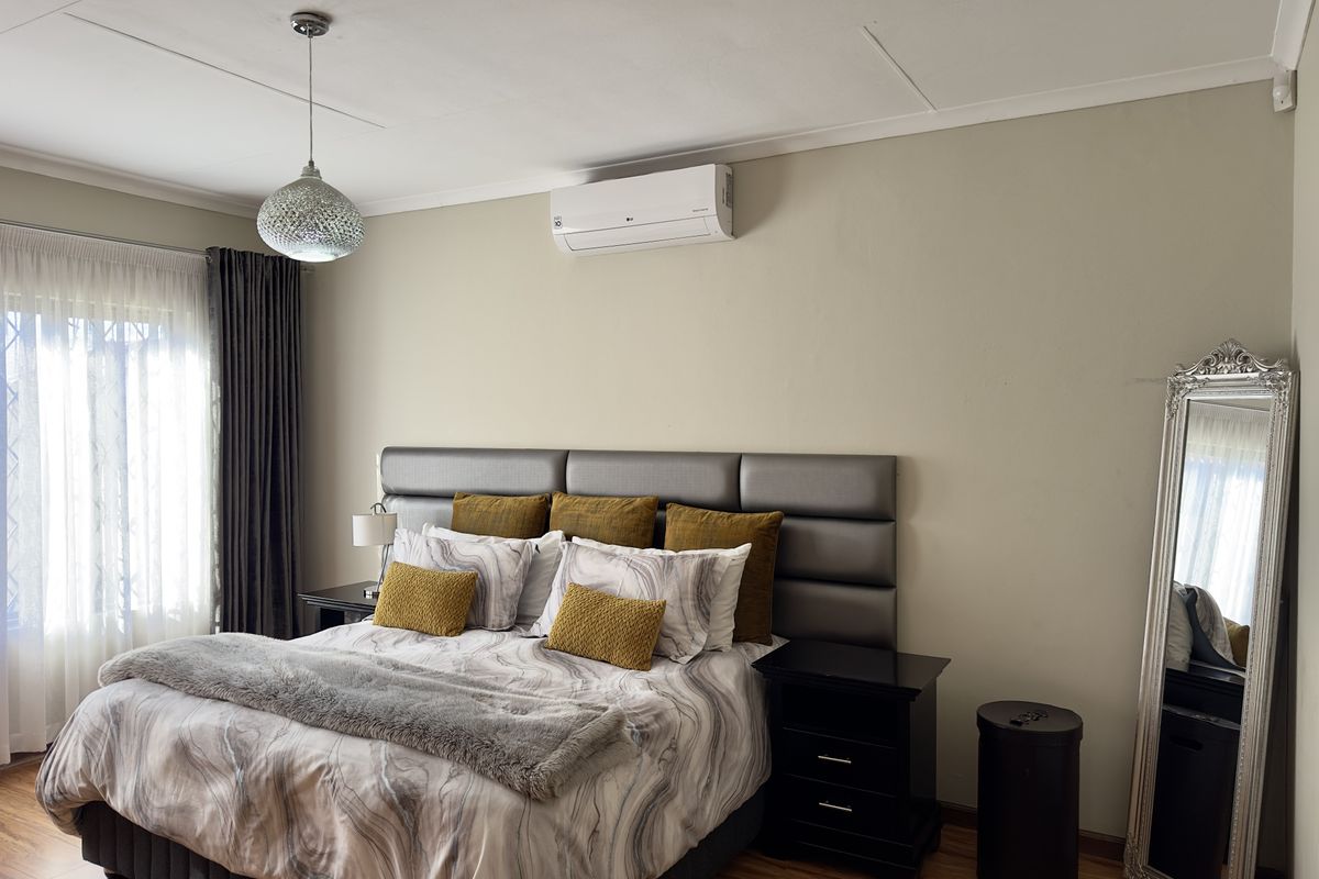 A well-maintained bedroom featuring wood-look flooring, a wall-mounted air conditioning unit, and a modern pendant light fixture.
