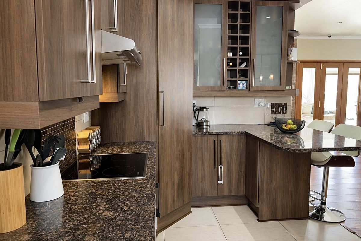 Modern kitchen featuring dark wood cabinetry, granite countertops, a built-in electric hob, extractor fan, and a breakfast bar area.