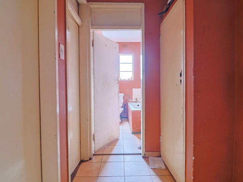 A narrow hallway featuring tiled flooring and built-in cupboards, providing access to an adjacent bathroom with a bathtub.