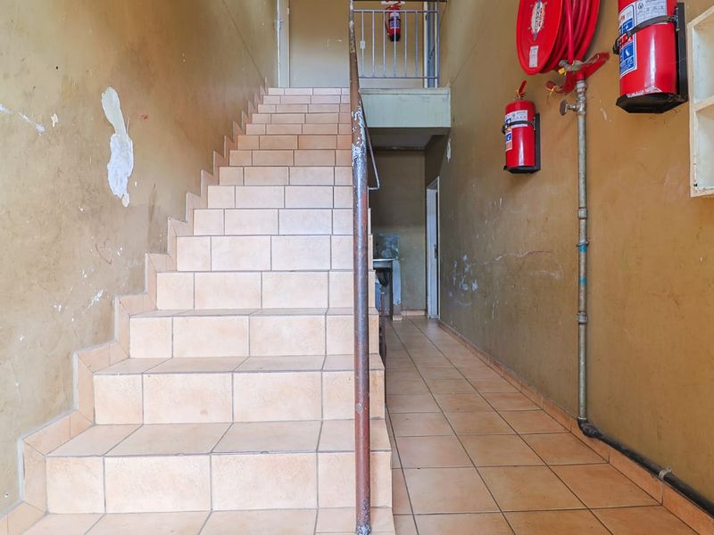 A utilitarian hallway featuring a tiled staircase, metal handrail, and wall-mounted fire safety equipment, showing signs of wear and requiring cosmetic maintenance.