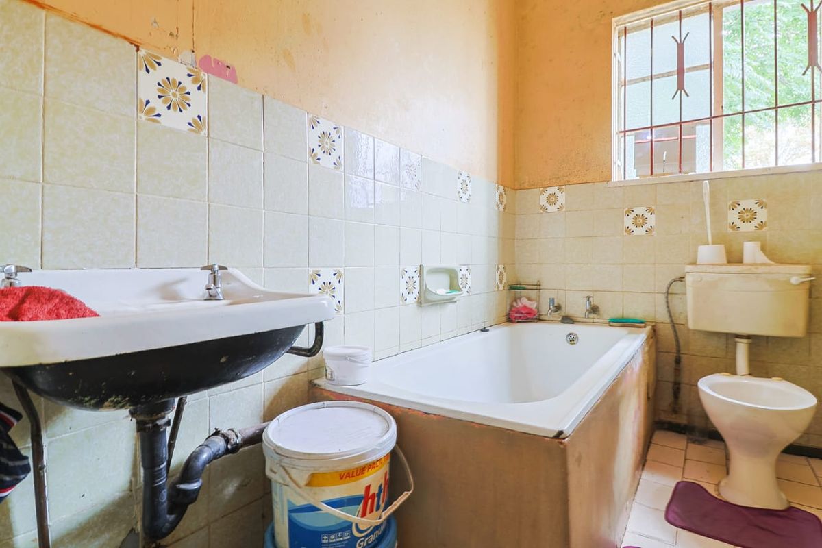 A dated bathroom featuring a pedestal sink, built-in bathtub, and toilet, requiring significant renovation and cosmetic updates to improve its condition and functionality.