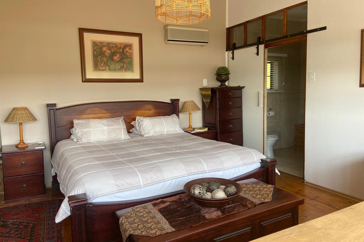 A well-maintained bedroom featuring hardwood flooring, an integrated air conditioning unit, and a sliding barn door providing access to an en-suite bathroom.