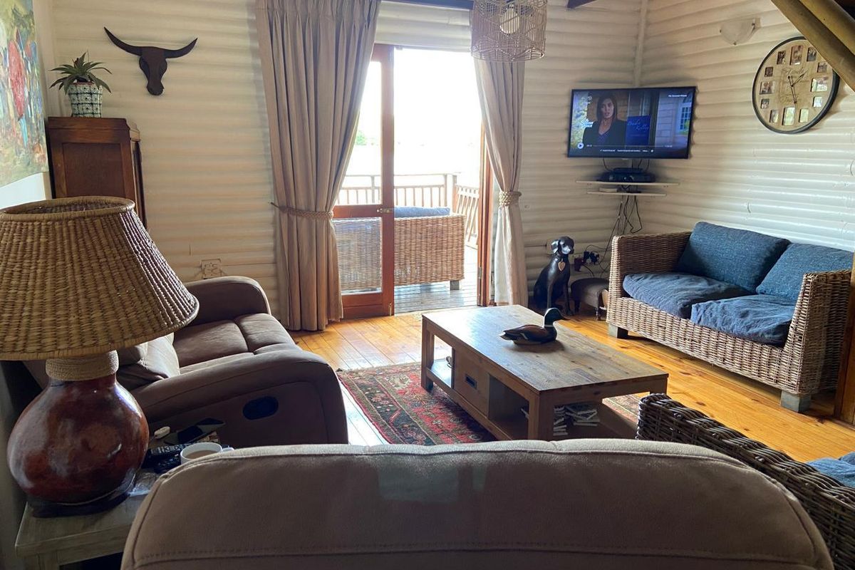 Cozy living room featuring rustic timber log walls, exposed ceiling beams, hardwood flooring, and direct access to an outdoor deck area.