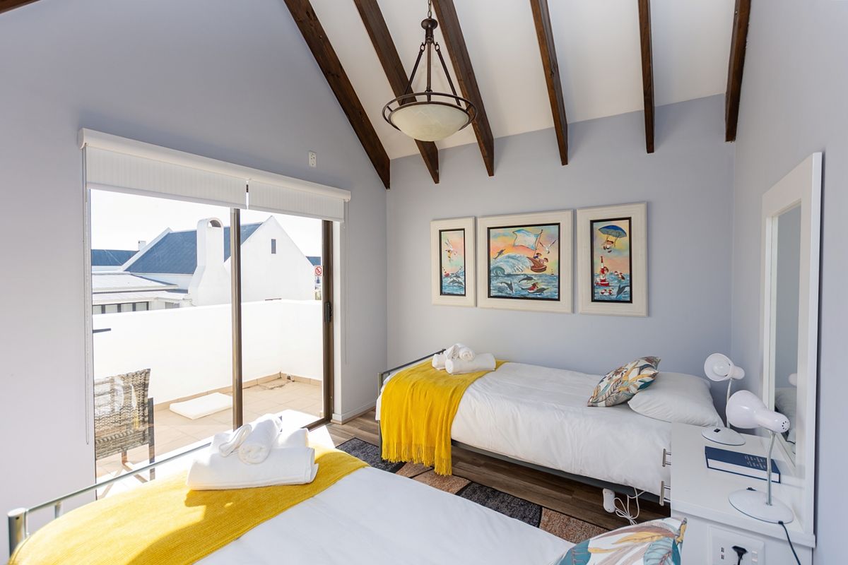 A bright bedroom featuring exposed timber ceiling beams, laminate flooring, and a sliding glass door providing direct access to a private balcony.