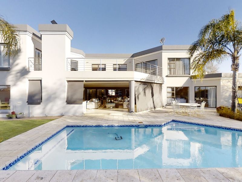 Rear elevation of a modern two-story house featuring a swimming pool, paved patio area, and an upper-level balcony with stainless steel railings.