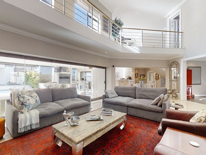 Spacious double-volume living room featuring a mezzanine level, stainless steel balustrades, a modern freestanding fireplace, and large sliding doors opening to the outdoor area.