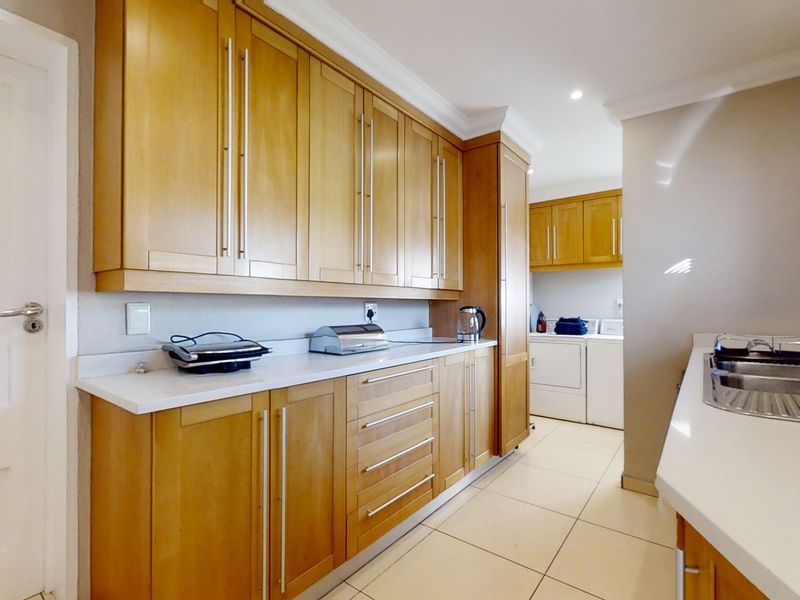 A functional scullery featuring timber cabinetry, stone countertops, and a stainless steel sink, providing additional workspace and storage adjacent to the main kitchen area.